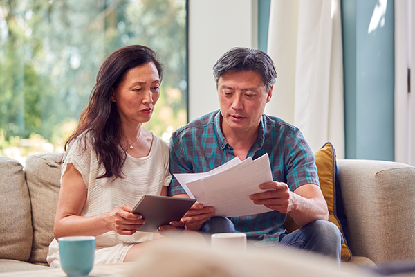 middle-aged Asian couple sitting on the living room couch looking at their financial documents